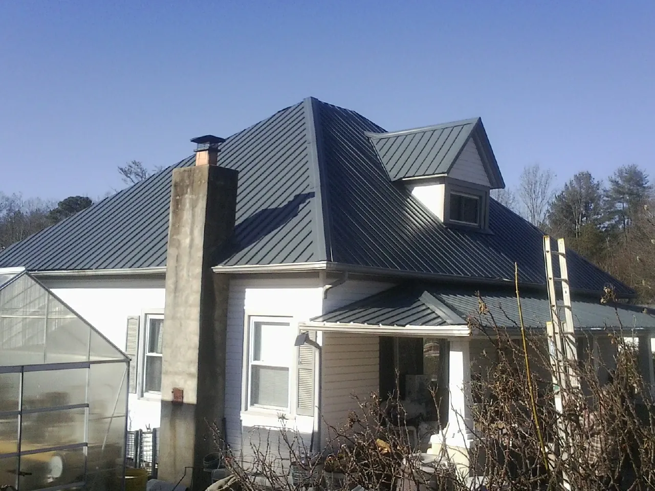 Dark blue standing seam metal roof on a white farmhouse with dormer — Slate & Tile Roof Repair by Roofing Brothers in Conehatta