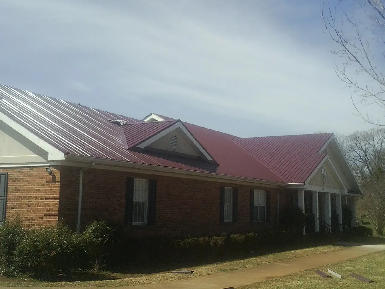 Red metal roof with gabled entries on a long brick building, from a Hail Damage Roof Repair job in Conehatta