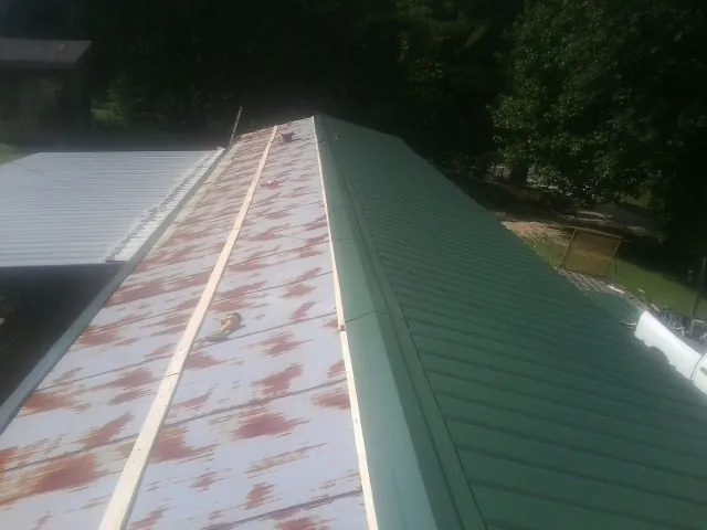Old rusted panels beside newly installed green metal roofing — Wind Damage Roof Repair by Roofing Brothers in Conehatta
