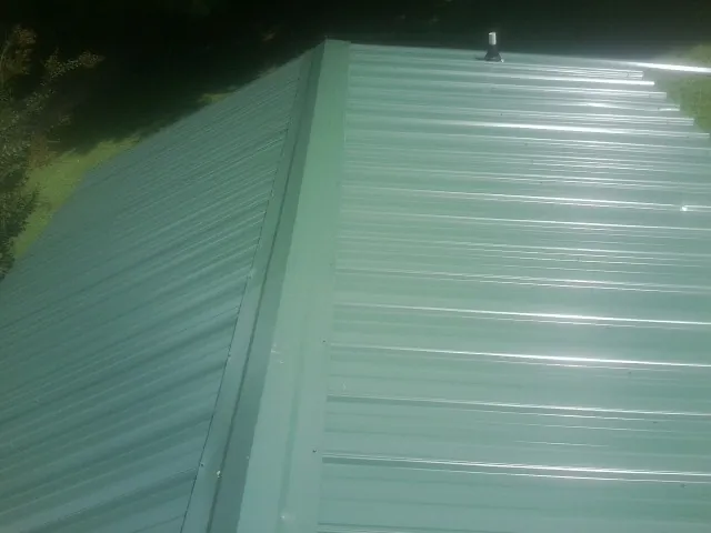 New green metal panels meeting at the ridge of a roof — Flat Roof Repair work by our crew in Conehatta