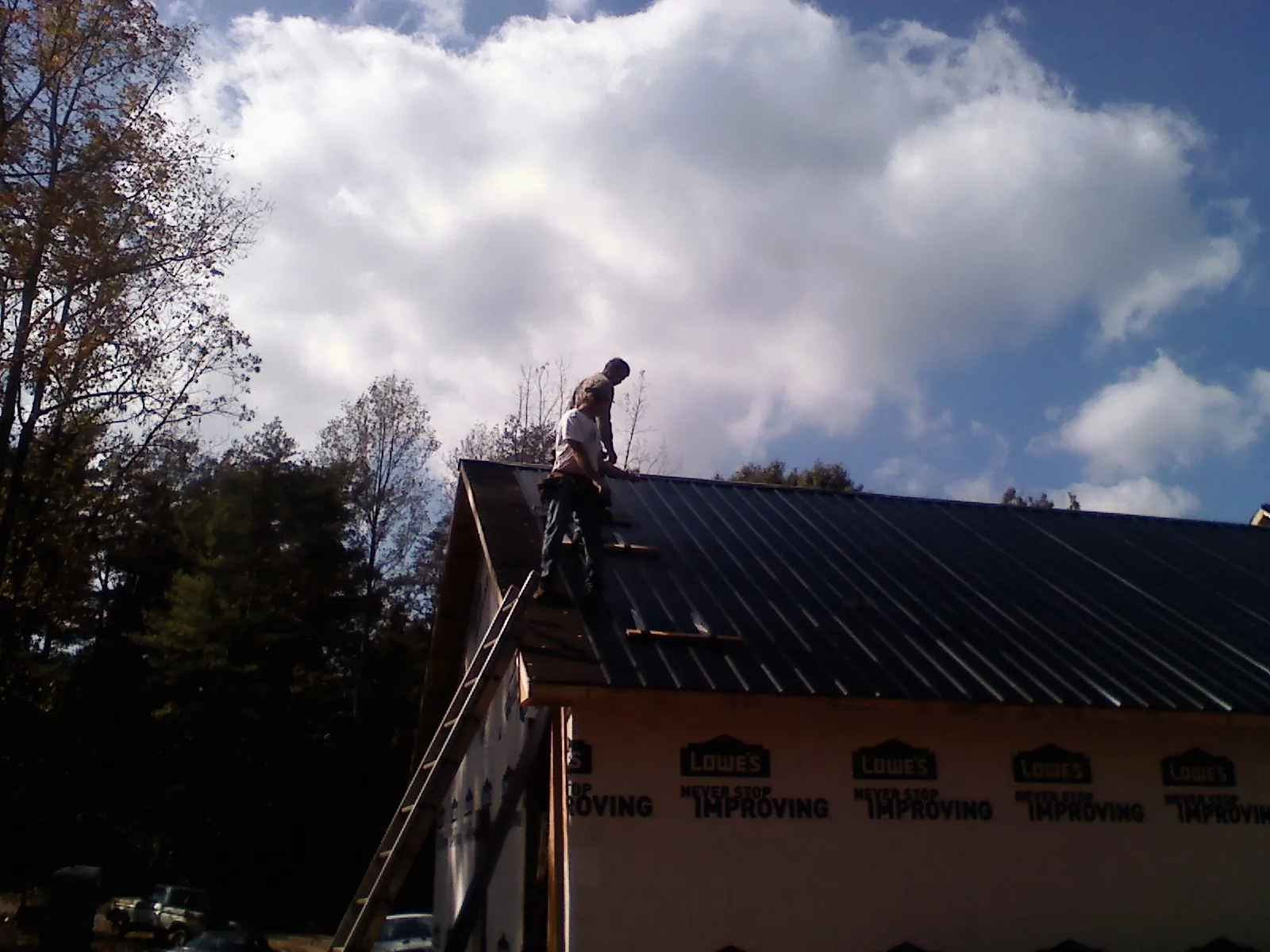 Roofer fastening dark metal panels high against a cloudy sky, from a Roof Inspection job in Conehatta