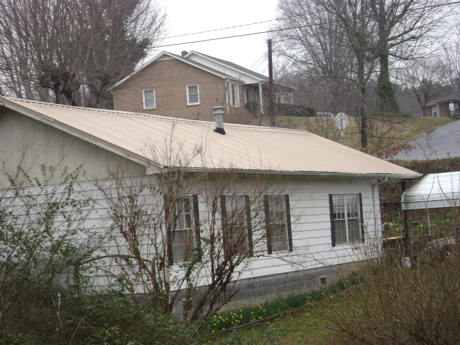 Tan metal roof on a white sided house set into a hillside — Commercial Roofing by Roofing Brothers in Conehatta