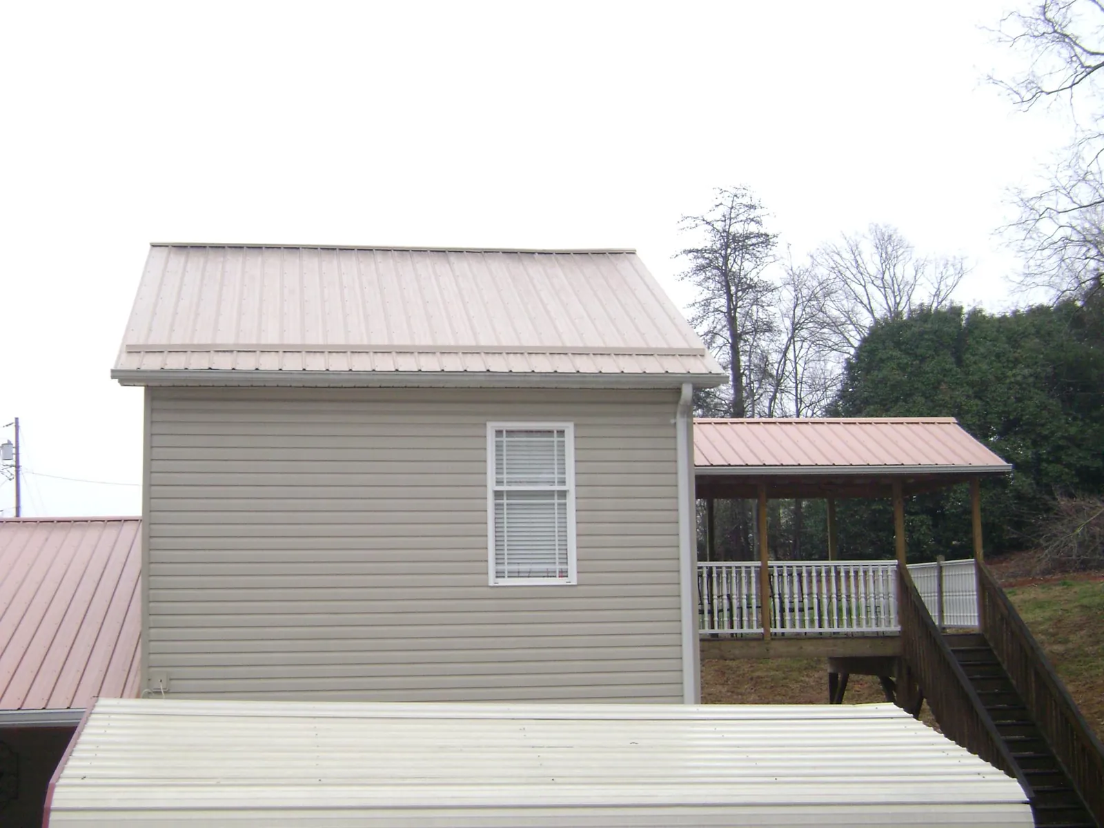 Tan metal roofs on a two story addition and attached porch, from a Roof Replacement job in Conehatta